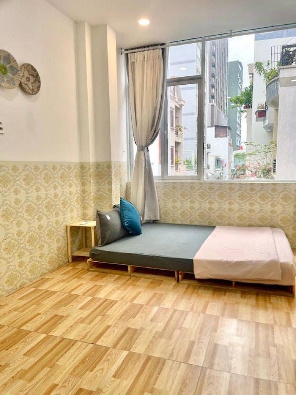 A room with a bed, a small table, a window with curtains, and patterned wallpaper.