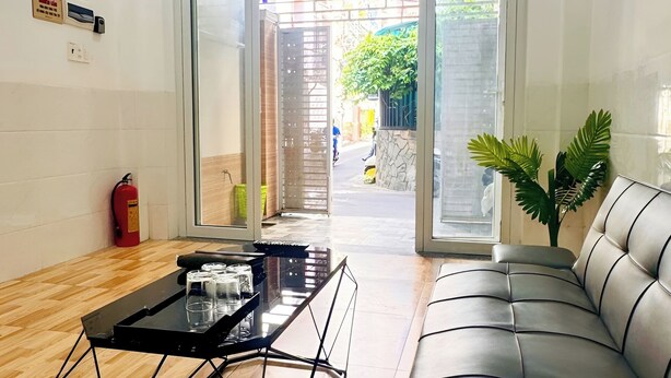 Un área de recepción con entrada por puerta de vidrio, una mesa de centro de metal negro, un sofá de cuero y una planta en maceta.