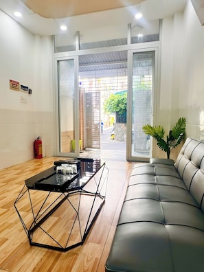 A reception area with a glass door entrance, a black metal coffee table, a leather sofa, and a potted plant.
