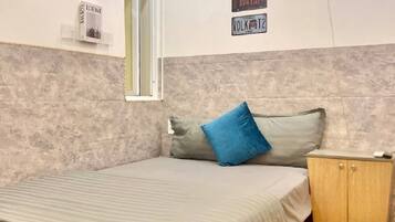 A bedroom with a bed, a nightstand, a window, and wall decorations including license plates and a neon sign.