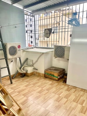 A room with a tiled floor, an air conditioning unit, a fan, a window with bars, and a ladder.