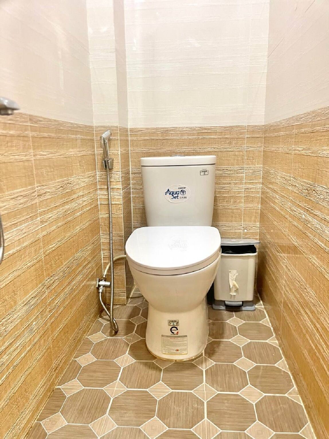 A bathroom with a toilet, a trash bin, and a shower.