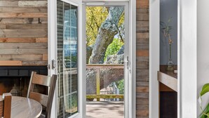 A room with a wooden wall, a glass door leading outside, a table with chairs, and a small plant on a shelf. - Live Oak Beach House (Isle of Palms)