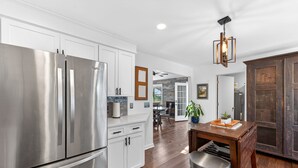 A modern kitchen with stainless steel appliances, white cabinetry, and a wooden dining table. - Live Oak Beach House (Isle of Palms)