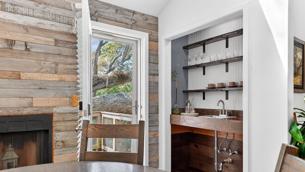 A dining area with a wooden table and chairs, a fireplace, and a kitchen with wooden shelves and a sink. - Live Oak Beach House (Isle of Palms)