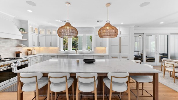 Uma cozinha moderna com armários brancos, uma ilha grande com banquetas e duas luminárias pendentes de vime.