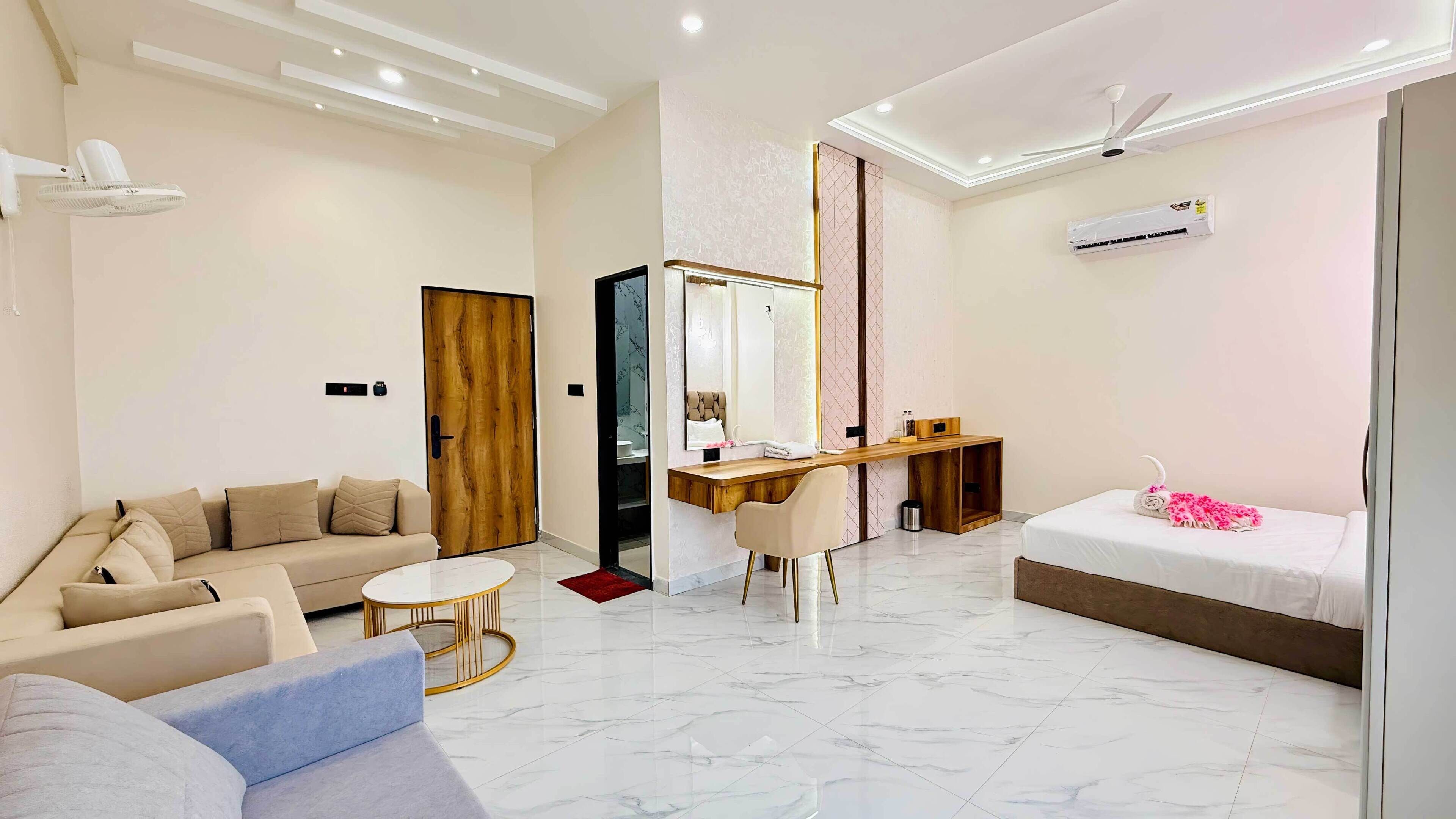 A modern hotel room with a sofa, a desk, a bed, and a bathroom.