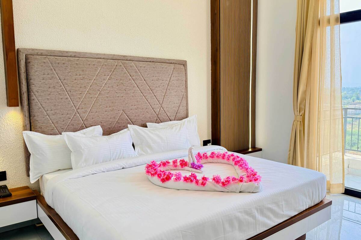 Habitación de hotel con cama, cabecera, mesita de noche, ventana con vistas y cortinas.
