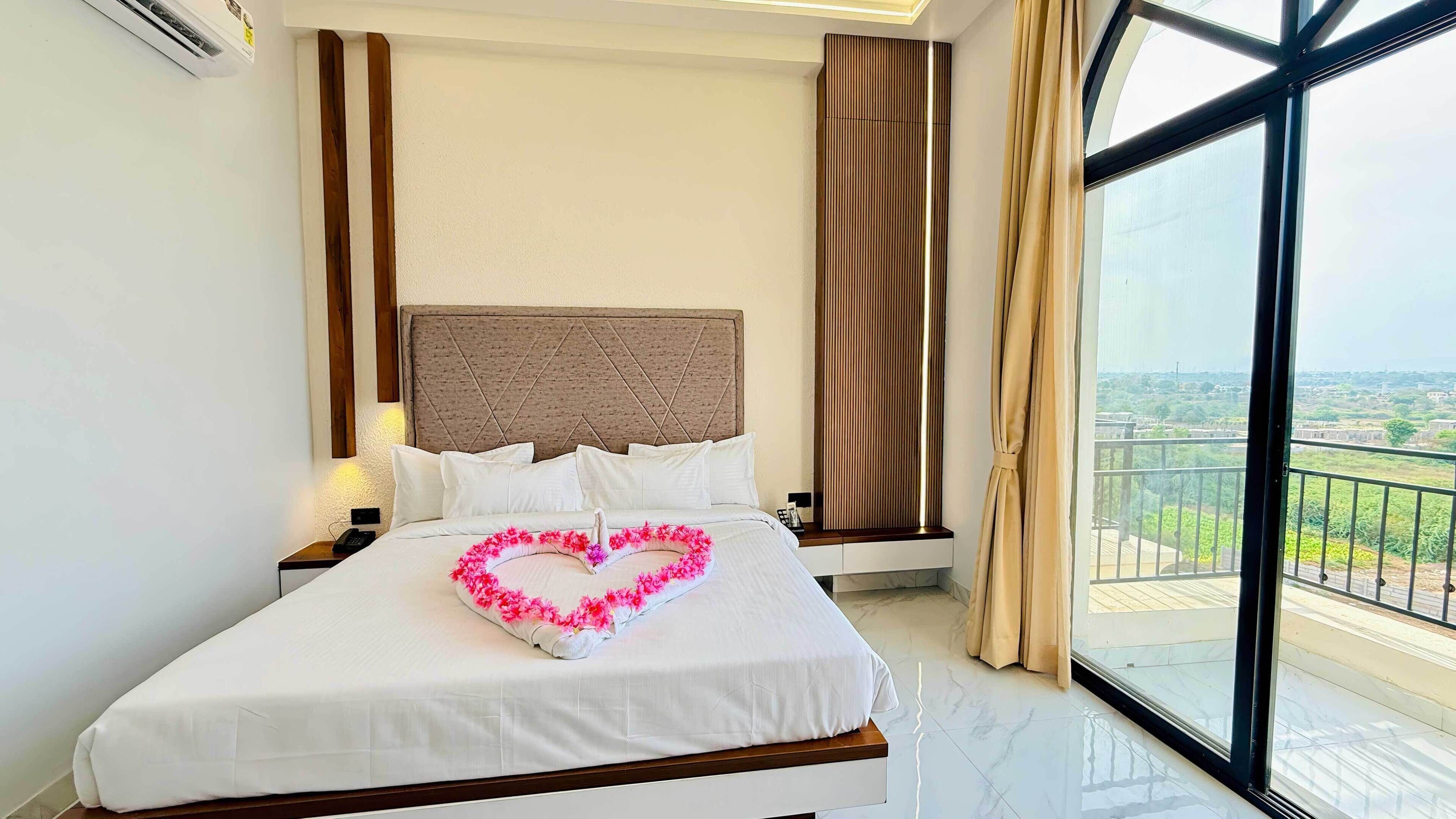 A hotel room with a large bed, a headboard, a nightstand, a window with a view, and a curtain.