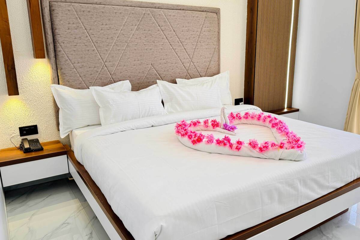 Habitación de hotel con una cama grande, cabecera de madera, mesita de noche con teléfono y ventana con cortinas.
