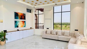 A spacious room with a large window, a sofa, a cabinet, and abstract art on the wall.