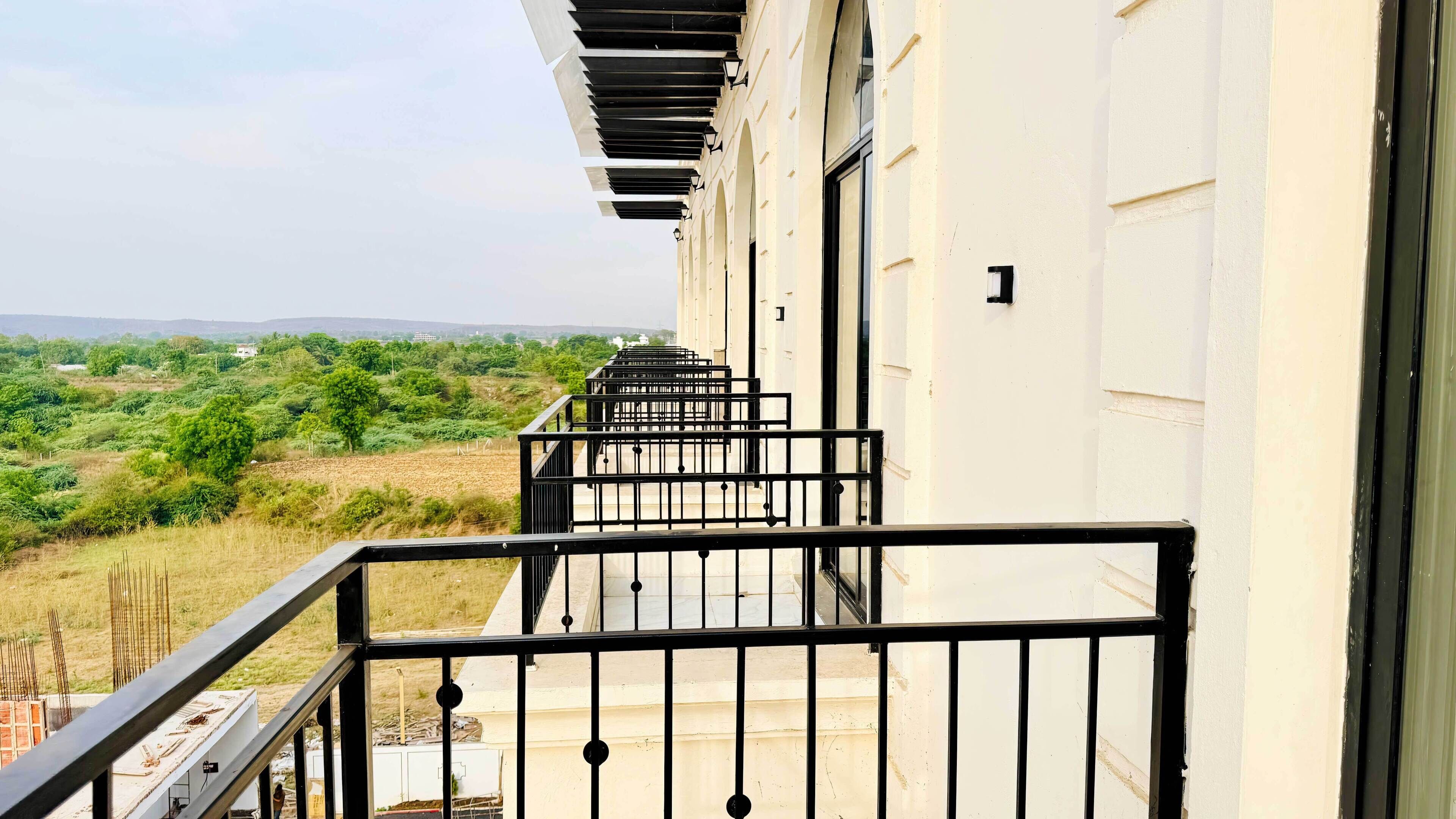 A balcony with a metal railing, a white building, and a view of a green landscape.
