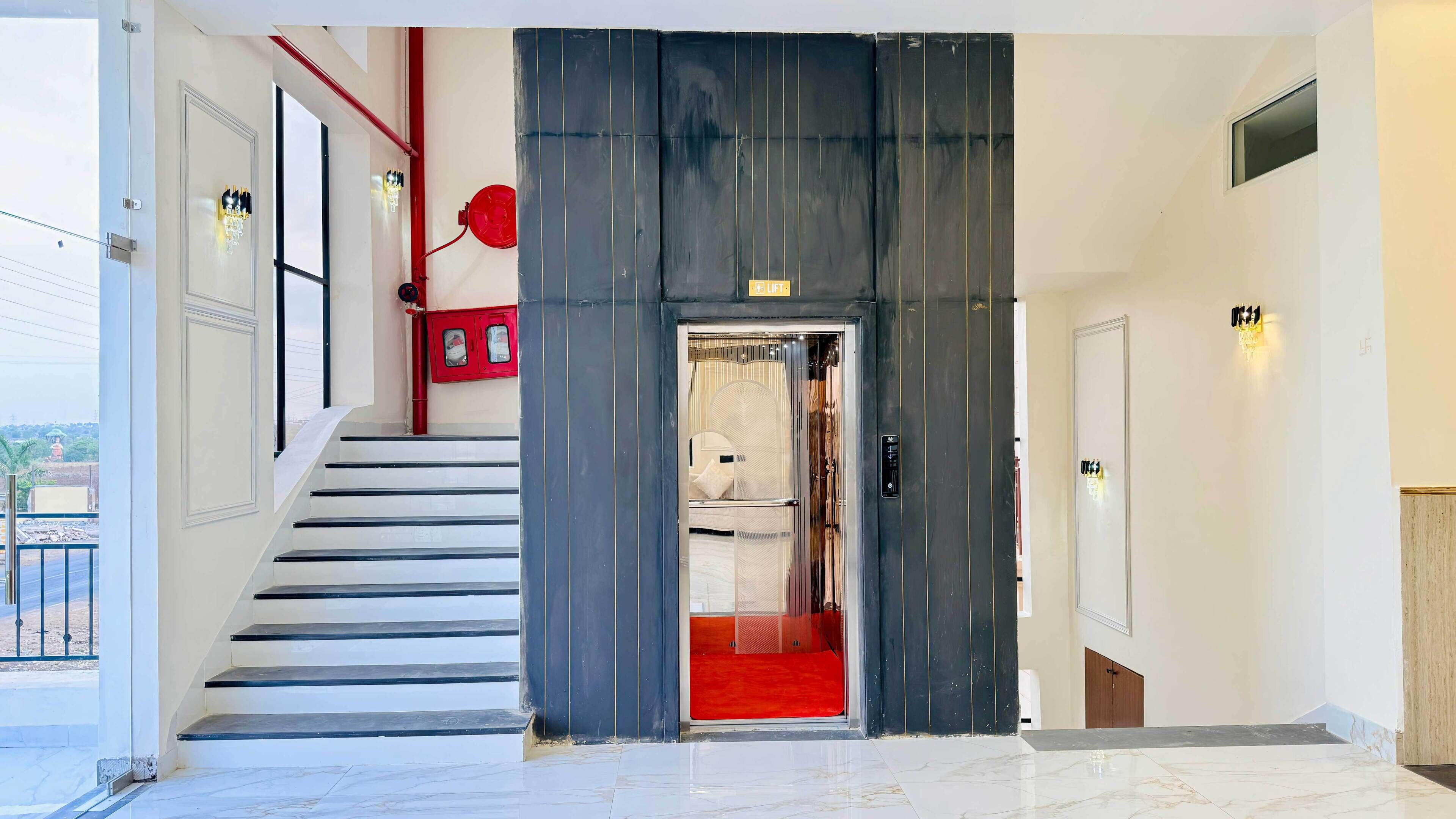 A modern hotel entrance with a staircase, a red carpet, and a glass elevator door.