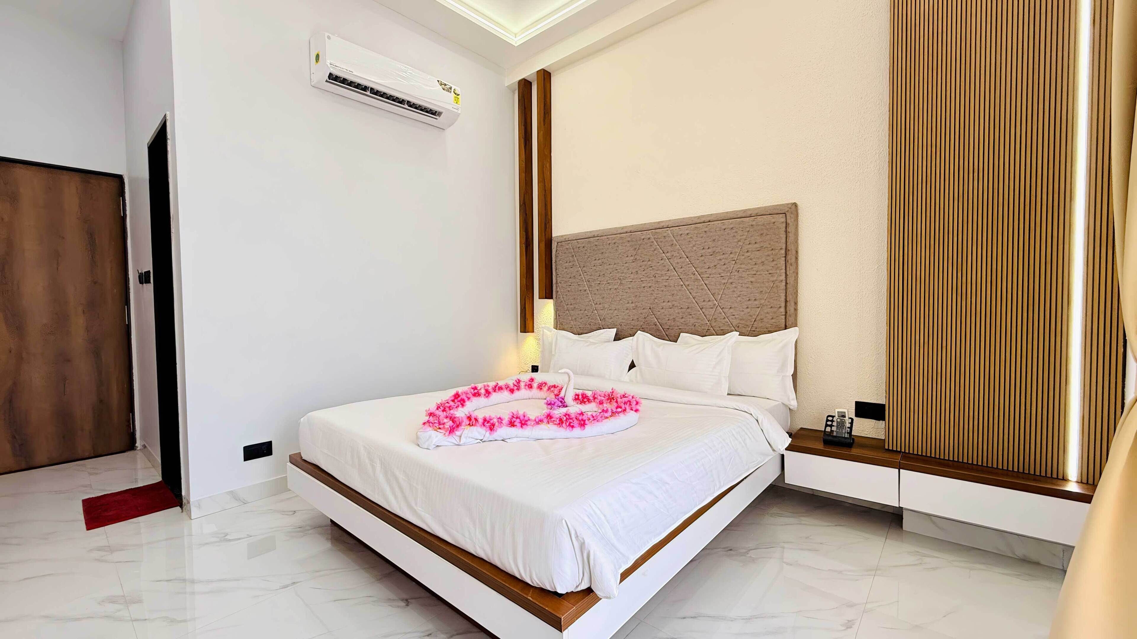 A hotel room with a bed, a wooden headboard, a red accent wall, a white air conditioning unit, and a wooden door.