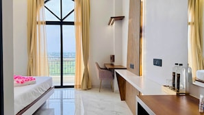 A modern hotel room with a balcony, a bed, a desk, and a chair.
