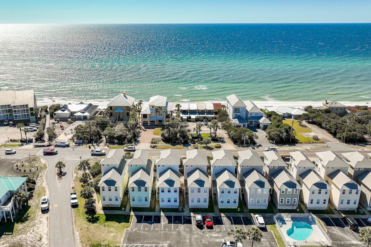 A coastal residential area with a row of houses, a parking lot, and a swimming pool.