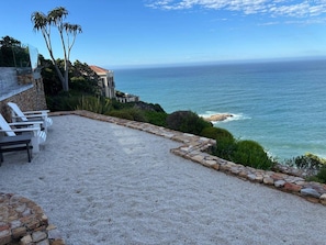 Une terrasse avec des chaises blanches, un mur en pierre et une vue sur l’océan.