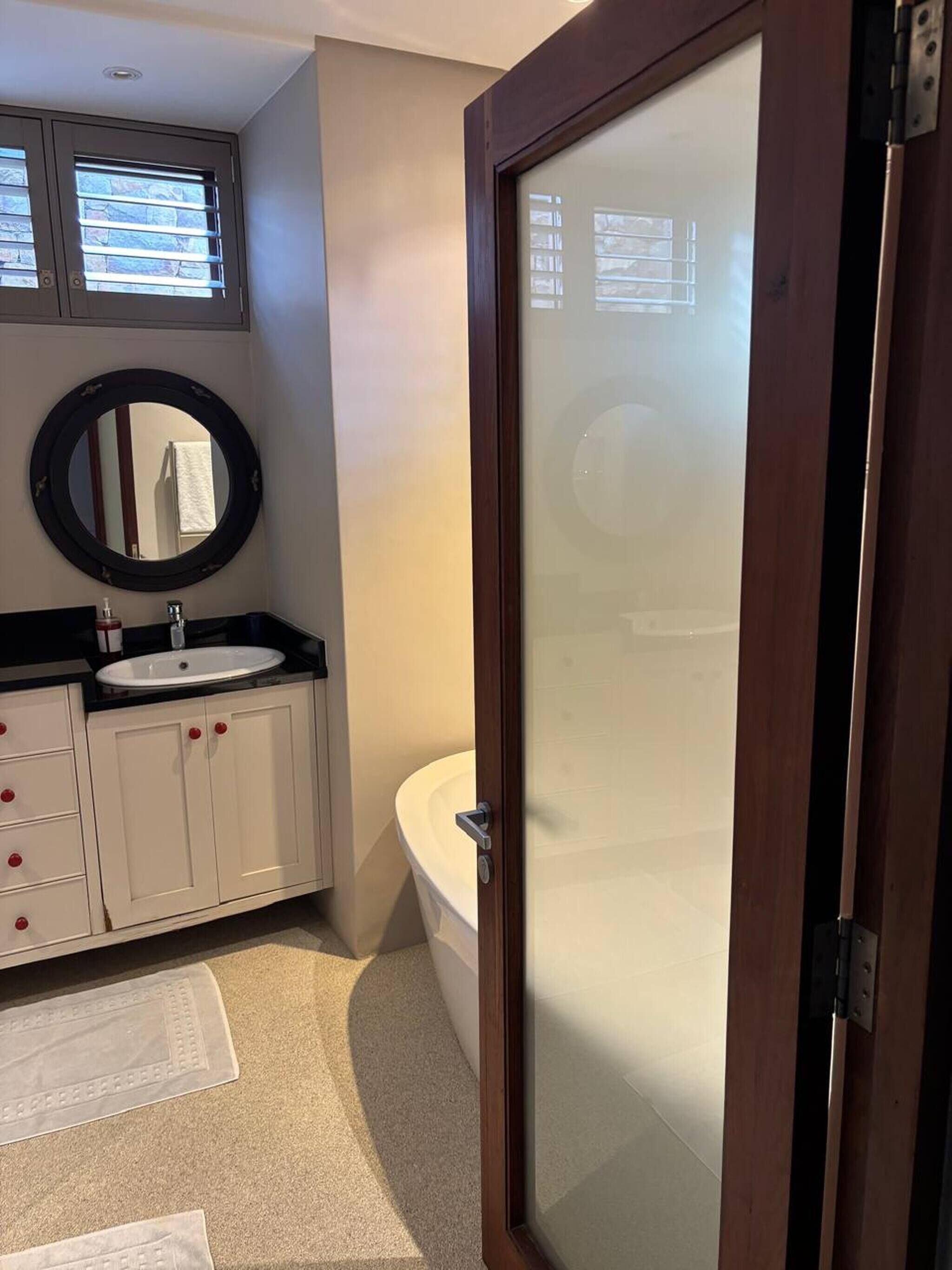 A bathroom with a white sink, a round mirror, a toilet, and a frosted glass door.