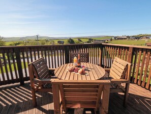 Een houten terras met een ronde tafel en stoelen, een fles champagne en een bord eten.