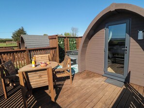 Een houten terras met een eettafel, een overdekte zithoek en een deur naar een beschutgedeelte.
