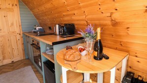 A wooden interior with a kitchen area, including a wooden table with a bottle, glasses, and food items. - Fern Folly (Whitby)