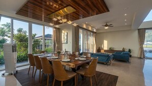 Un espace de repas moderne avec une table et des chaises en bois, un ventilateur de plafond et de grandes fenêtres donnant sur l’extérieur.