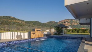 Une piscine agrémentée d’une cascade, entourée d’une clôture et offrant une vue sur des collines.