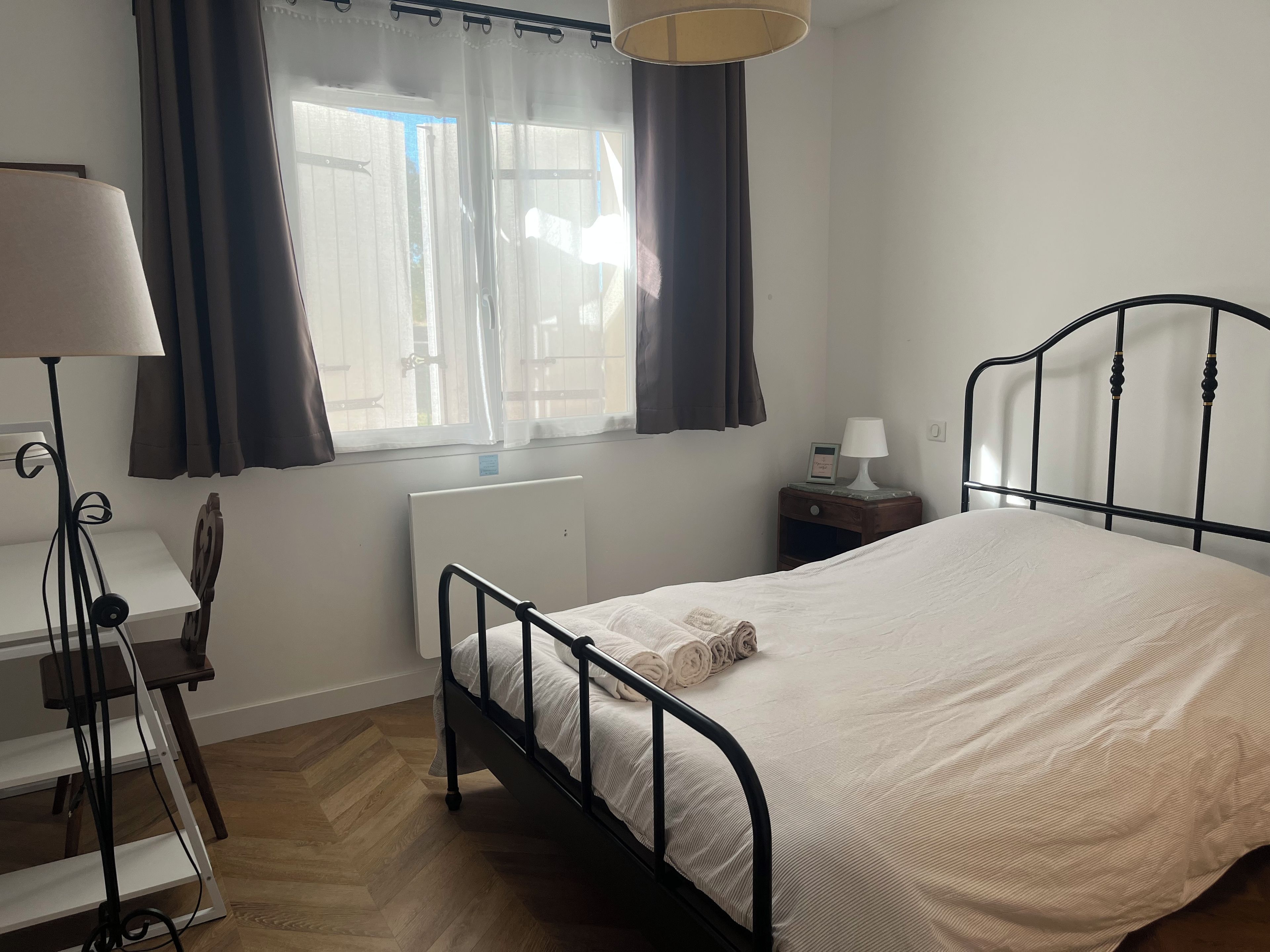 Un dormitorio con cama, mesita de noche, lámpara y ventana con cortinas.