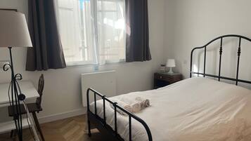 Un dormitorio con cama, mesita de noche, lámpara y ventana con cortinas.