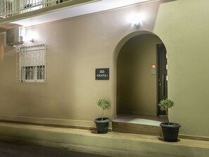An entrance with a sign reading 'ARRAPAJ APARTMENTS,' two potted plants, and a window with bars. - Rapai City Apartments - Central Stays in Zakynthos Town (Zakynthos)