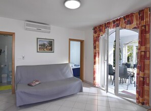 Ein Wohnzimmer mit einer Couch, einem Gemälde, einer Klimaanlage und einer Glastür zum Außenbereich.