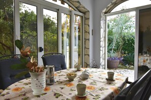Ein Wintergarten mit gedecktem Tisch für zwei Personen, umgeben von Stühlen und Blick auf den Garten.