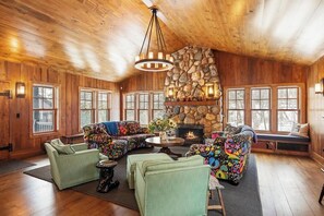 A cozy cabin interior with a stone fireplace, wooden walls, and large windows.