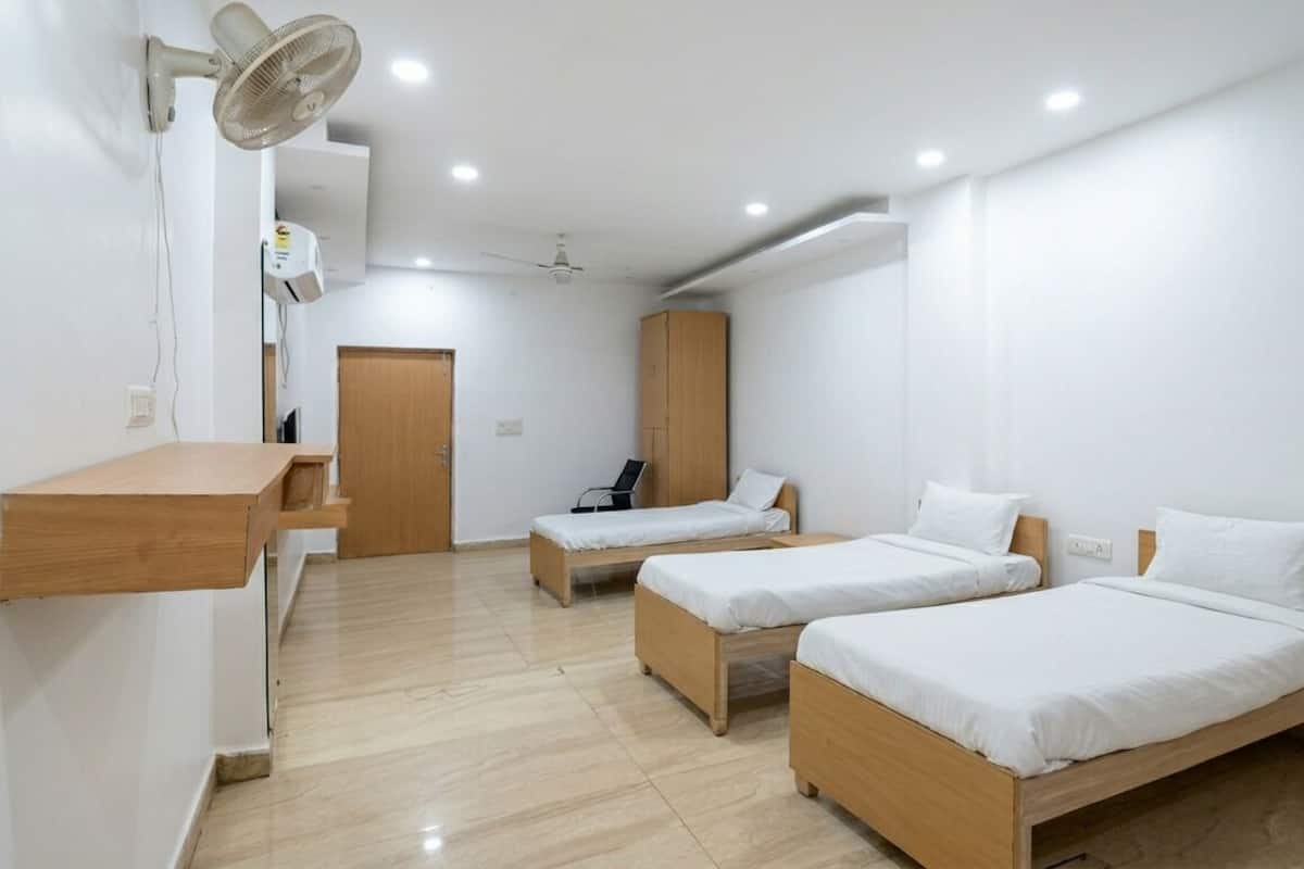 Una habitación con tres camas de madera, un escritorio, un ventilador de pared y un ventilador de techo.