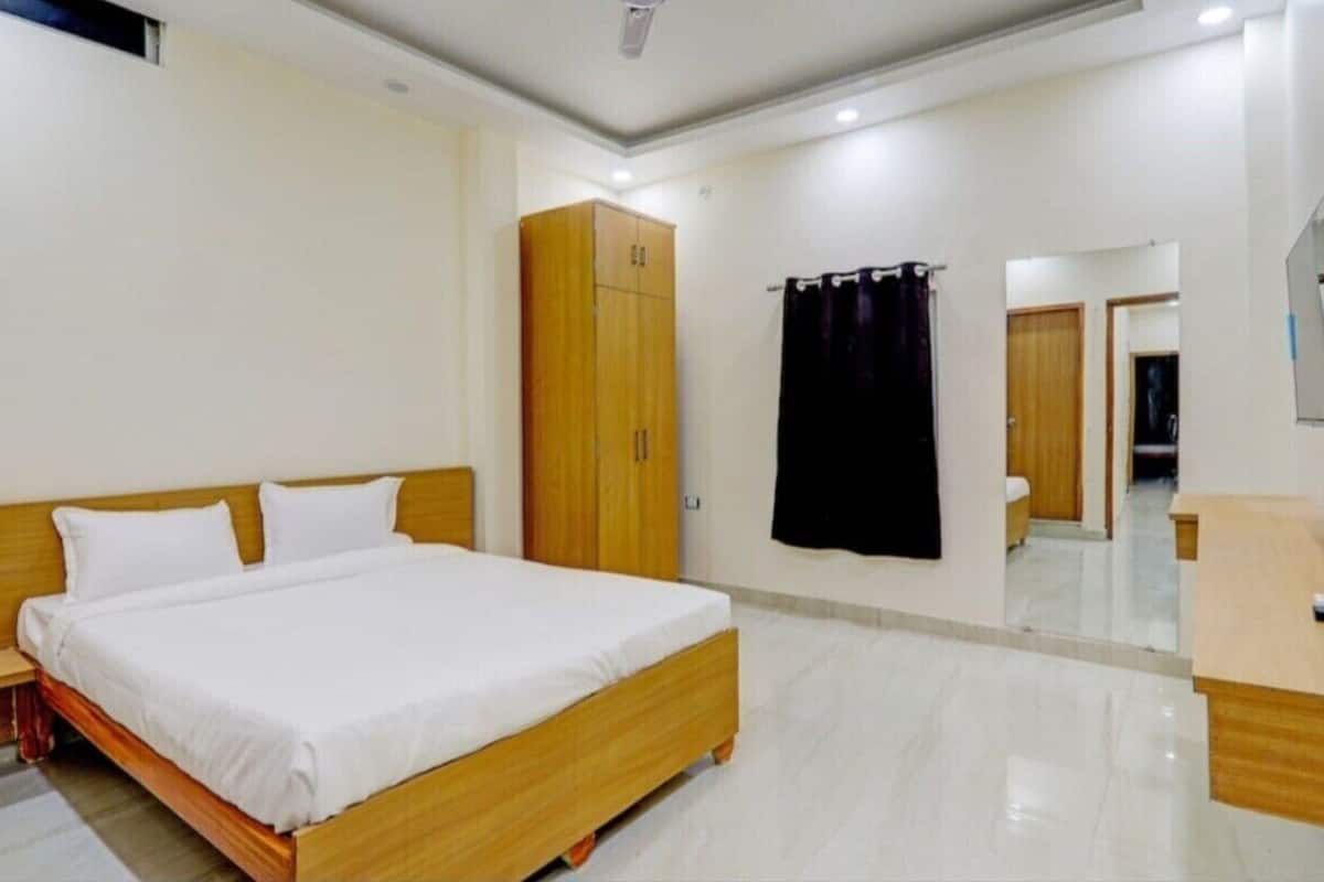 Un dormitorio con cama de madera, un armario, un espejo y un baño visible a través de una puerta abierta.