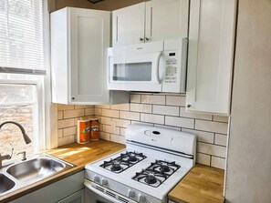 Una cocina con armarios blancos, microondas, estufa y ventana con persianas.
