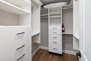Ein begehbarer Kleiderschrank mit weißen Regalen, Schubladen und einem Feuerlöscher.