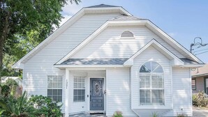 A single-story house with a front porch, a dark-colored front door, and a small garden area with various plants.