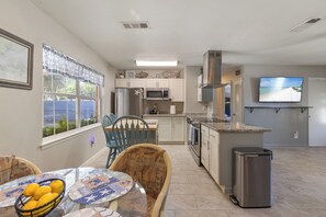 A modern kitchen with a microwave, refrigerator, and stainless steel appliances. There is a dining area with a table and chairs, and a TV mounted on the wall. - Perfect for families and groups! Enjoy a spacious home with a screened patio, fire pit, and kid-friendly yard. Prime location near the Science Center and main roads. Flexible beds make it ideal for extended stays. Comfort and connection await! (Fort Walton Beach)