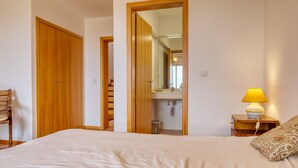 Ein Schlafzimmer mit einem Bett, einem Holzschrank, einem Spiegel, einem Nachttisch mit Lampe und einem gemusterten Kissen.