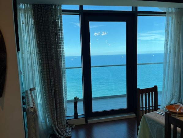Une pièce dotée d’une grande fenêtre donnant sur la mer, d’une table avec une chaise et d’une petite plante en pot.