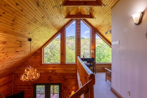 A wooden interior with large windows, a chandelier, and a staircase leading to an outdoor deck. - Highwood- Mountain Views, Hot Tub, Arcade, Fire Pit, Foosball, Sleeps 12 (Boone)