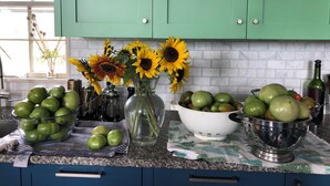 Una cucina con mobili verdi, una parete a mosaico in marmo e diversi tipi di frutta e verdura sul bancone.