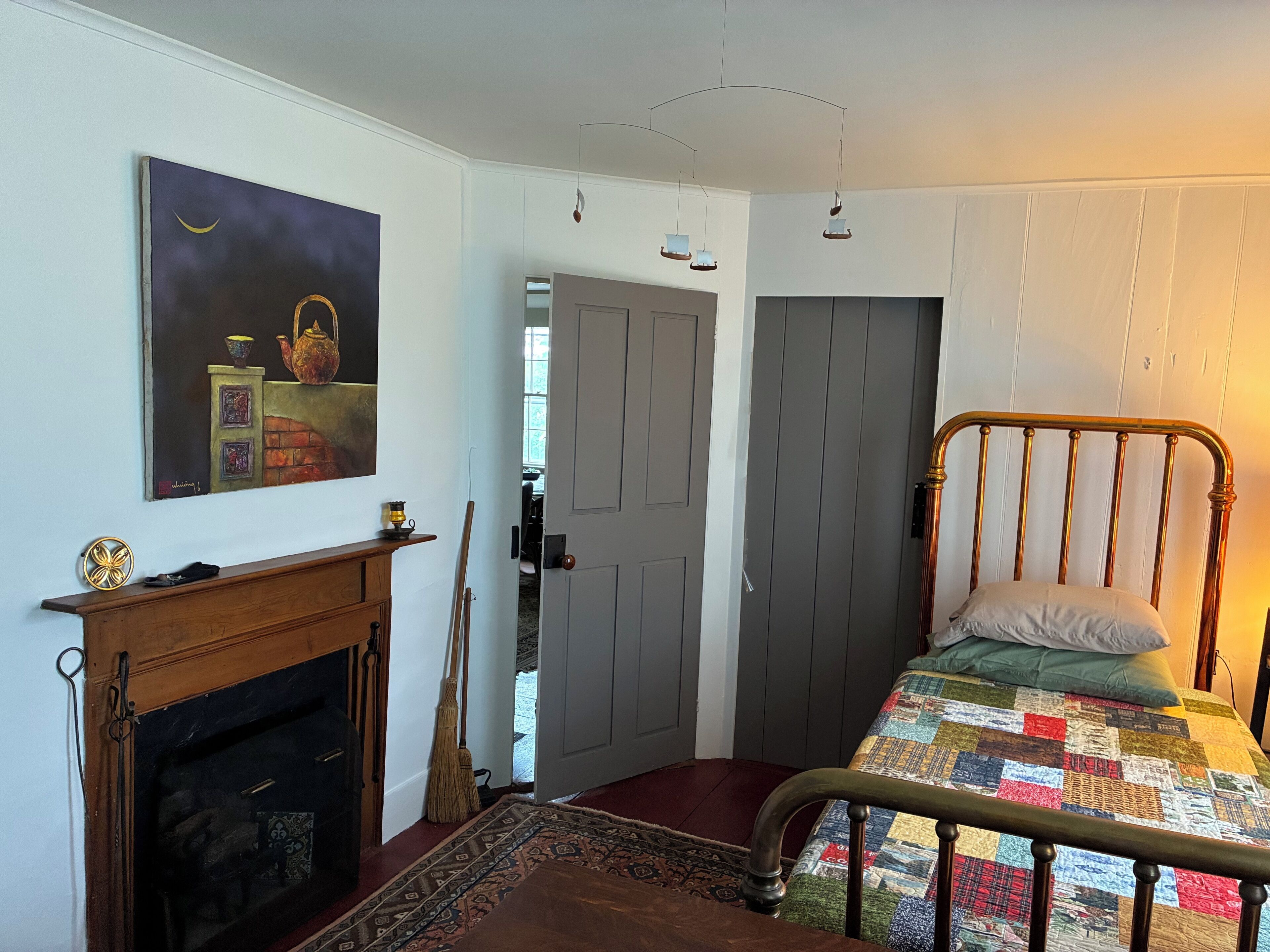 Une chambre à coucher avec un lit, une cheminée, un tableau et une porte donnant sur une autre pièce.