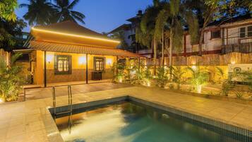 A swimming pool with a tiled deck, a covered area with a tiled roof, and surrounding palm trees.