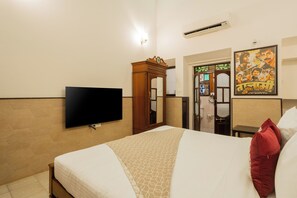 A hotel room with a bed, a flat-screen TV mounted on the wall, a wooden wardrobe, and a poster on the wall.
