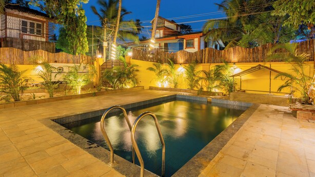 A swimming pool with a tiled deck, surrounded by a bamboo fence, and palm trees in the background. - Alaya Stays Casa do Mar Heritage 4BHK (Calangute)