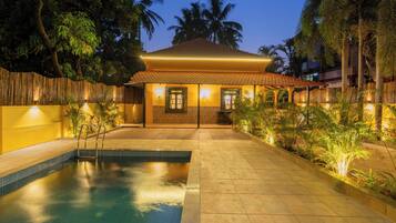 A pool area with a tiled deck, a wooden fence, and a building with a tiled roof and windows.