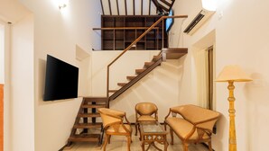 A staircase with wooden railings, a flat-screen TV mounted on the wall, and a seating area with chairs and a table. - Alaya Stays Casa do Mar Heritage 4BHK (Calangute)