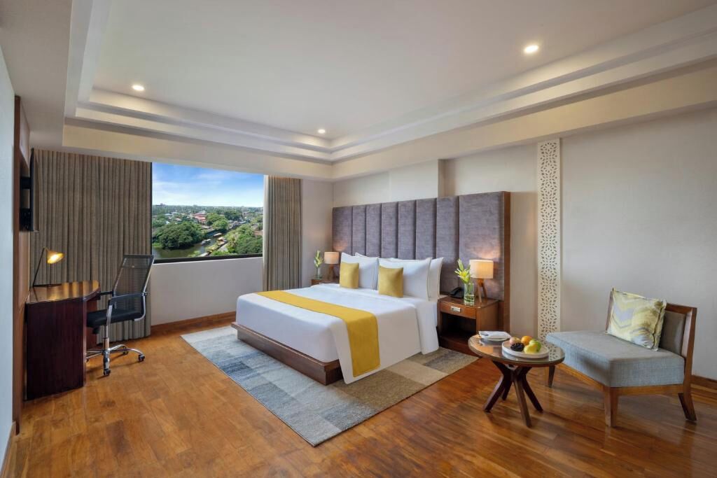 Habitación de hotel con una cama grande, un escritorio, una silla, una mesita con fruta y vistas a la ciudad.